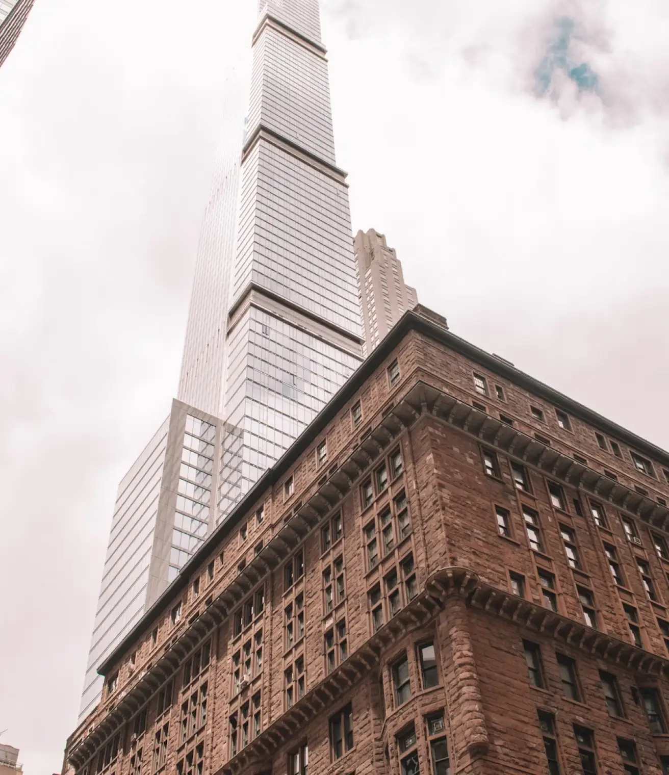 Photo looking up at a classic brownstone building with a modern skyscraper in the background